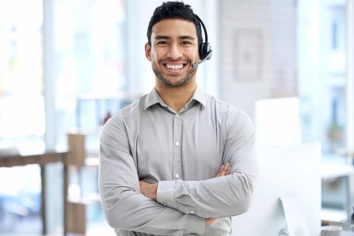 After PC support specialist training, a young technical support professional wearing a headset in an office.