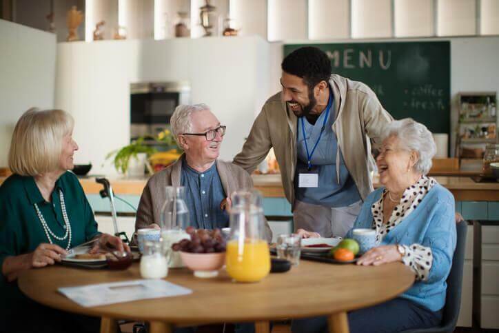 A smiling male community service worker interacting with senior citizens in a home after completing his community service worker training 