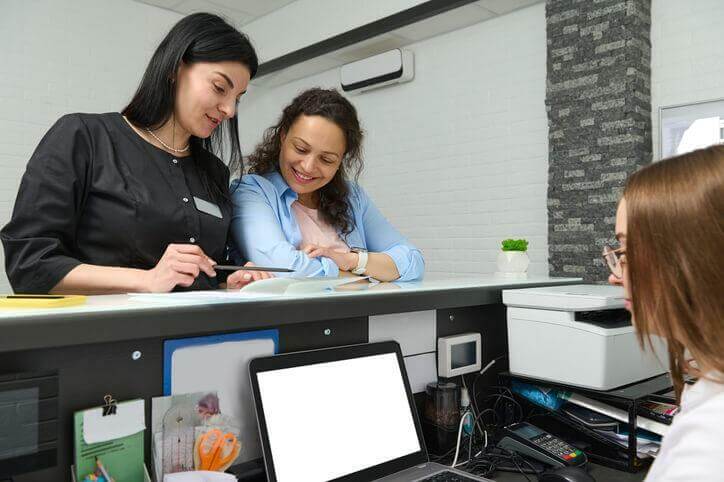 A career college graduate sitting at the front desk of a medical clinic helping patients 