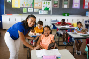 A smiling female Educational Assistant with a smiling female pupil in a classroom