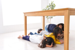 A group of students taking refuge under a desk under the supervision of an educational assistant in a classroom