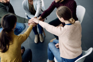 A community service and addictions worker joining hands in unity with clients during a session