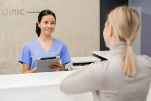 A medical office assistant greeting patients at a clinic reception desk