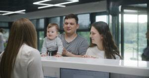 A pediatric clinic reception desk with a medical office assistant assisting a family