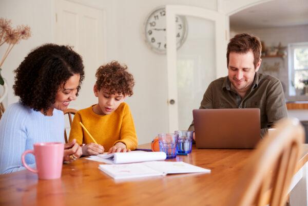 A parent studying online at home while helping a child with homework