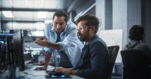 Network administrator explaining a technical issue to a non-technical colleague in an office setting